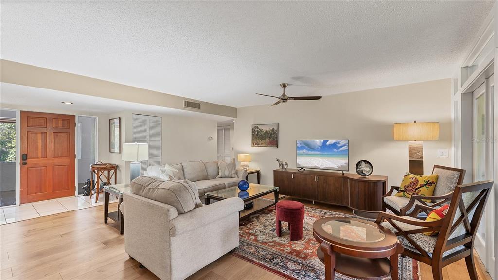 A living room features light wood flooring, a beige sofa, and a patterned area rug — 4957 CROSS CREEK ROAD UNIT 4957, SARASOTA, FL