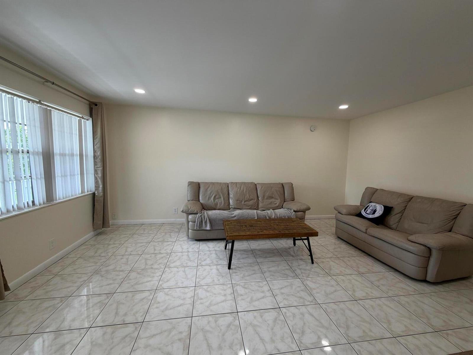 A living room features light-colored tile flooring, beige walls, two leather sofas, and a coffee table — 229 E Durham E # 229, Deerfield Beach FL 33442, DEERFIELD BEACH, FL