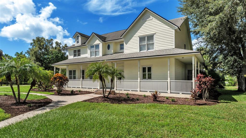 A two-story house with light yellow siding and a wrap-around porch under a blue sky — 1632 REGAL COVE COURT, KISSIMMEE, FL