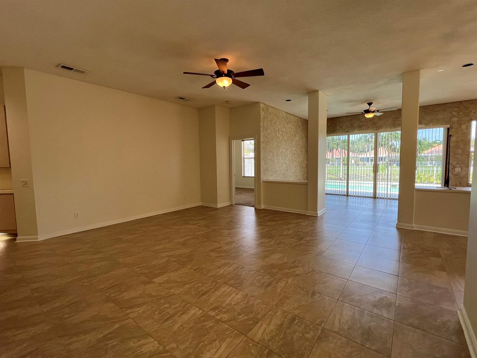 An open-concept living area features large tan floor tiles, two ceiling fans, and sliding glass doors — 244 Hampton Place, Jupiter FL 33458, JUPITER, FL