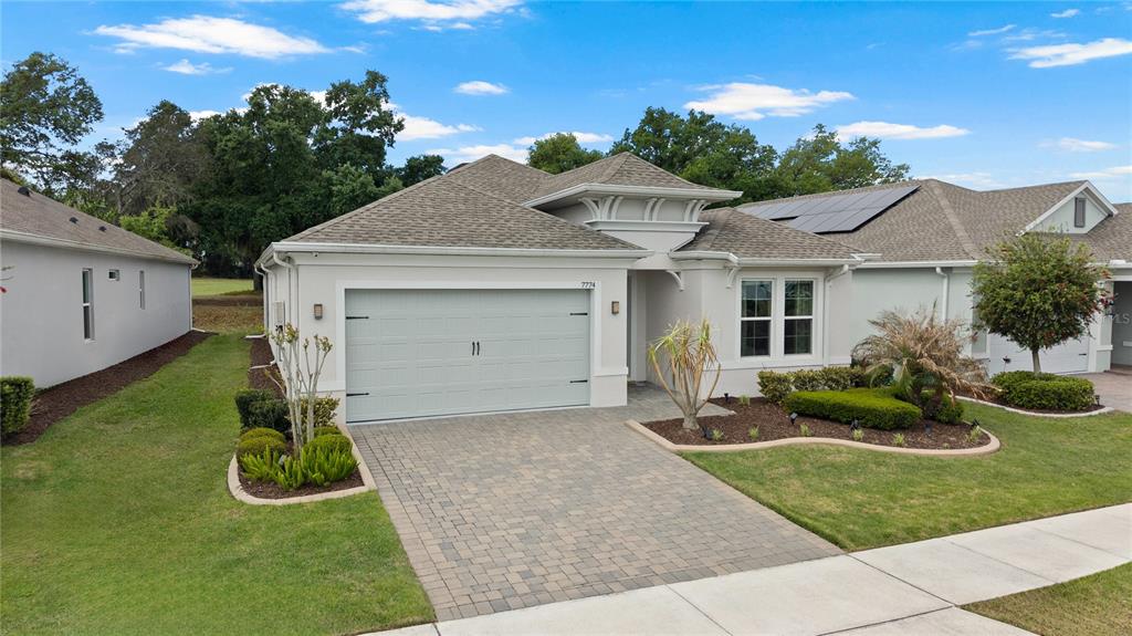 A single-story house features a light-colored stucco exterior, a paver driveway, and a two-car garage — 7774 FOUR SEASONS BOULEVARD, KISSIMMEE, FL