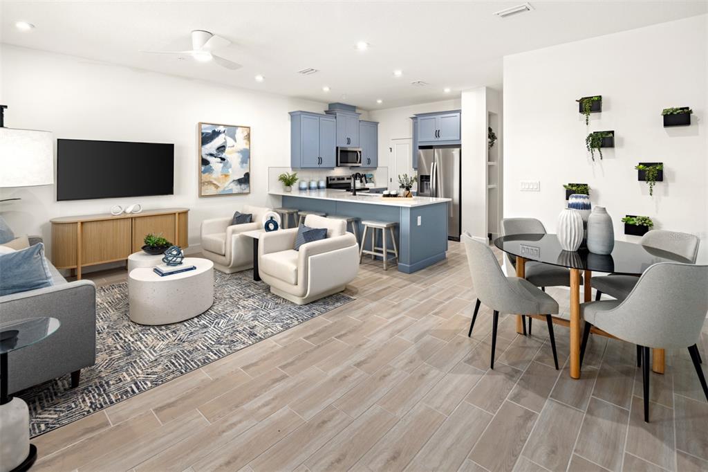 An open-concept living and dining area features blue kitchen cabinets, light wood-look tile floors, and furniture — 5132 GREENSHADE GROVE AVENUE, APOPKA, FL