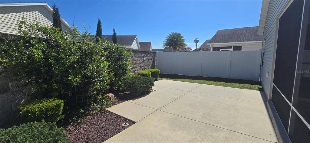 A concrete patio sits beside a house with a screened enclosure and a vinyl fence — 2577 LINDEWOOD STREET, THE VILLAGES, FL
