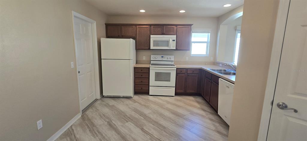 A kitchen with dark wood cabinets, white appliances, and light-colored wood-look flooring — 2577 LINDEWOOD STREET, THE VILLAGES, FL