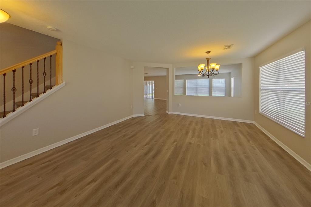 An empty living and dining area with wood-look flooring, a staircase, and a chandelier — 4667 CAVERNS DRIVE, KISSIMMEE, FL