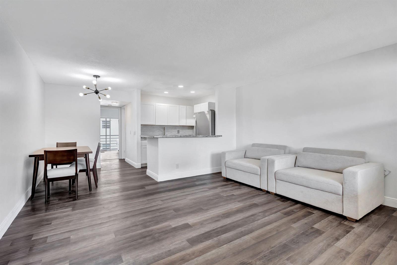 An open-concept living and dining area features light gray flooring, white walls, and a kitchen — 211 Sheffield I, West Palm Beach FL 33417, WEST PALM BEACH, FL