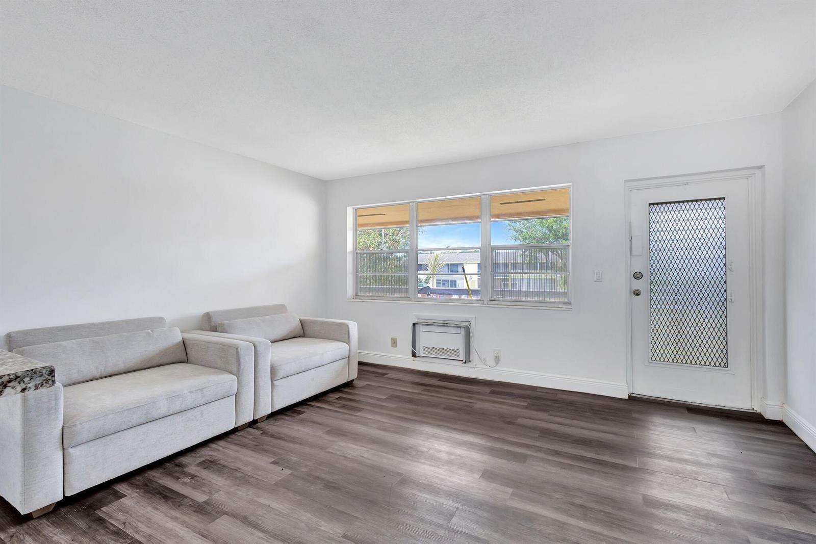 A living room features light gray sofas, dark wood-look flooring, and a window air conditioner — 211 Sheffield I, West Palm Beach FL 33417, WEST PALM BEACH, FL