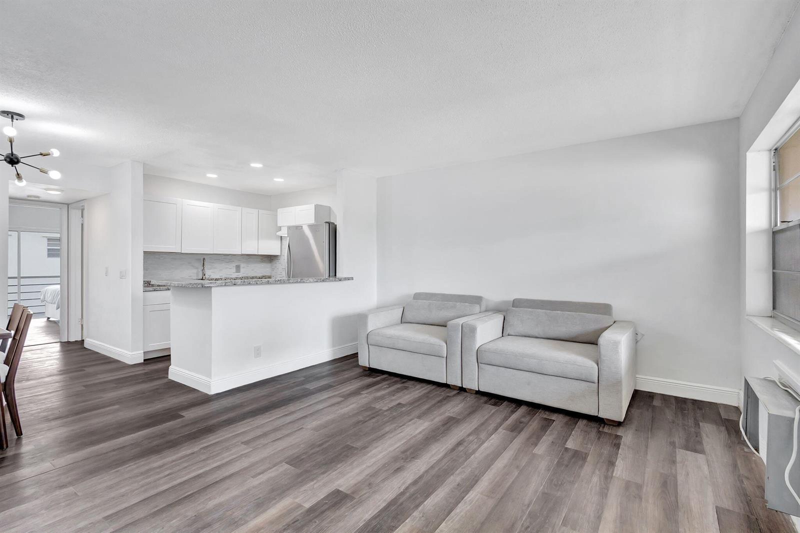 A living room with gray wood-look flooring, two light gray armchairs, and an open kitchen — 211 Sheffield I, West Palm Beach FL 33417, WEST PALM BEACH, FL