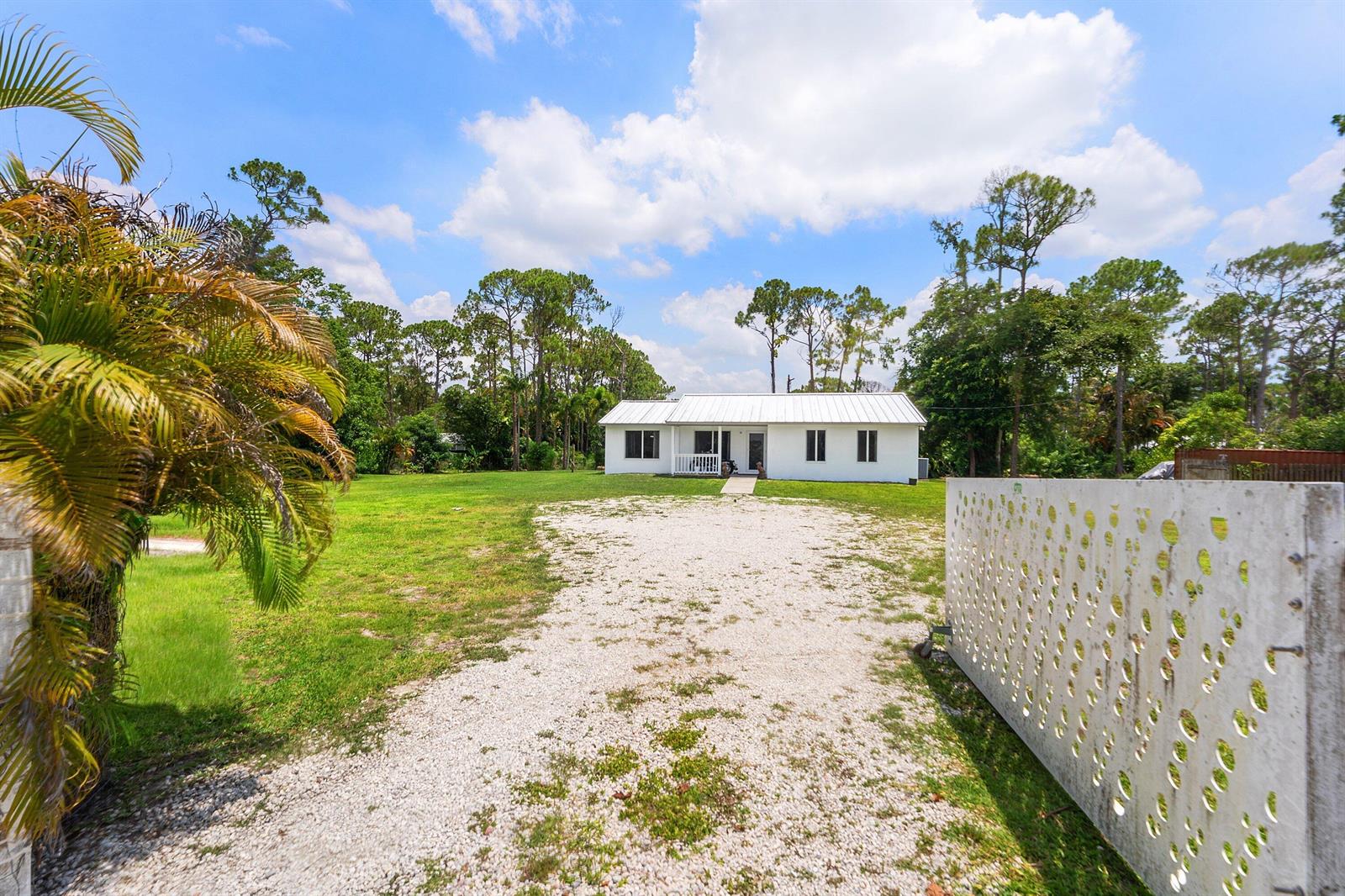 A white, single-story house sits at the end of a gravel driveway behind a fence — 12944 68th Street N, FL 33412, FL