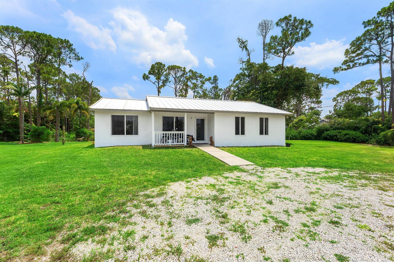 A white, single-story house with a metal roof sits on a large, grassy lot — 12944 68th Street N, FL 33412, FL