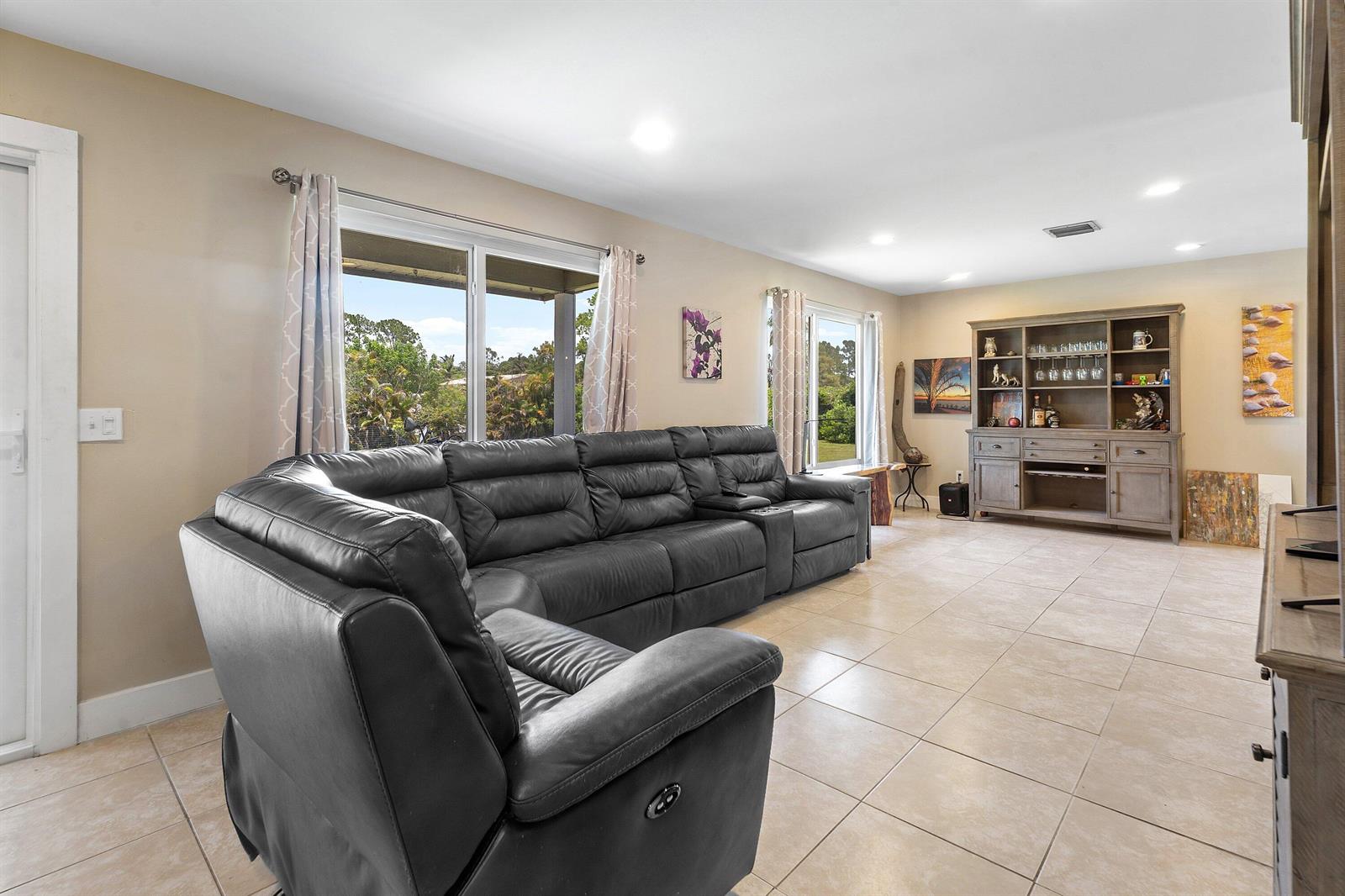 A living room features a large black leather sectional, tile flooring, and a wooden hutch — 12944 68th Street N, FL 33412, FL