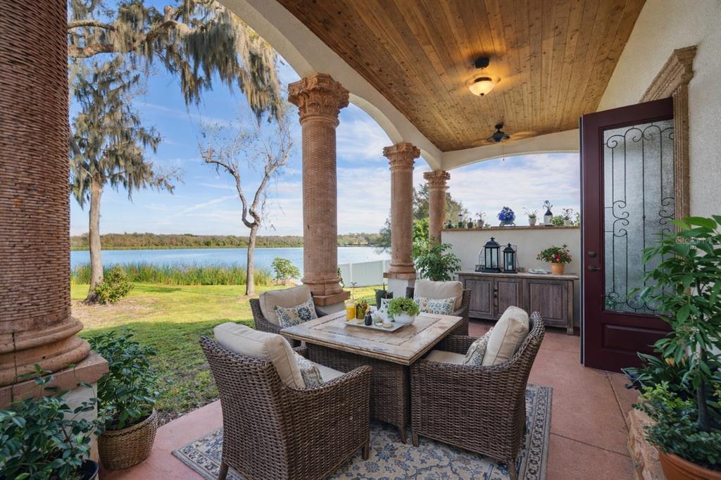 A covered patio features wicker furniture, stone columns, and a view of a lake — 775 CHRISTINA LAKE DRIVE, LAKELAND, FL