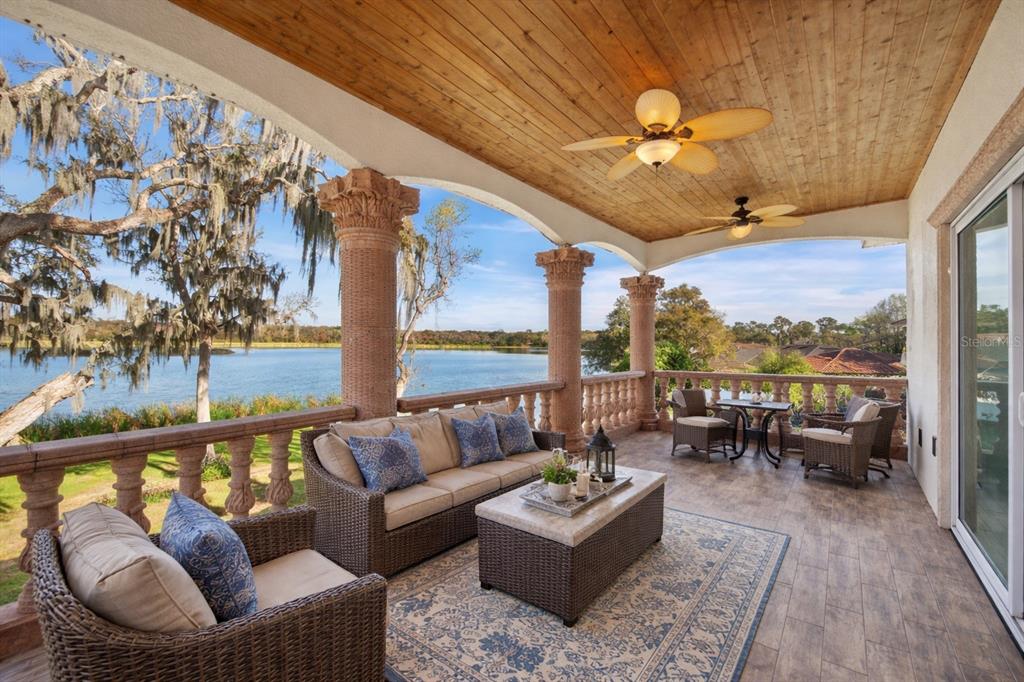 A covered outdoor patio features wicker furniture, stone columns, and a view of a lake — 775 CHRISTINA LAKE DRIVE, LAKELAND, FL