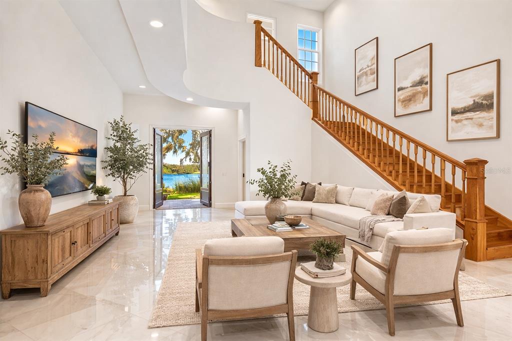 A bright living room features a wooden staircase, a sectional sofa, and a lake view — 775 CHRISTINA LAKE DRIVE, LAKELAND, FL