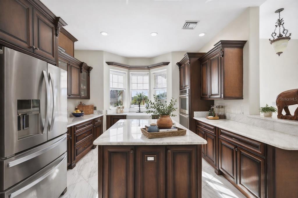 A kitchen features dark wood cabinetry, a central island with a stone countertop, and stainless-steel appliances — 775 CHRISTINA LAKE DRIVE, LAKELAND, FL
