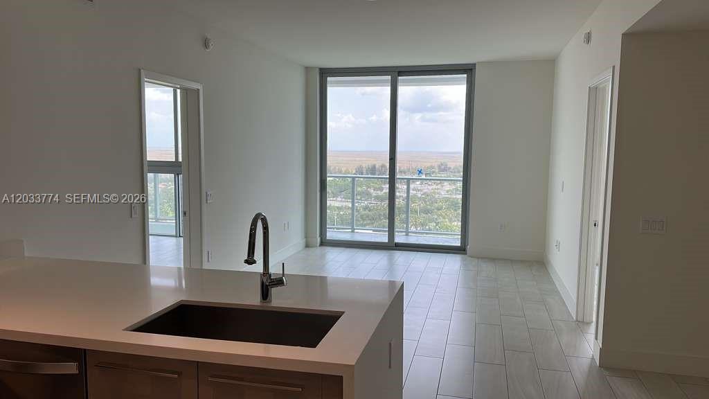 A modern kitchen island with a sink overlooks an open living area with balcony access — 2000 Metropica Way # 2111, Sunrise FL 33323, SUNRISE, FL