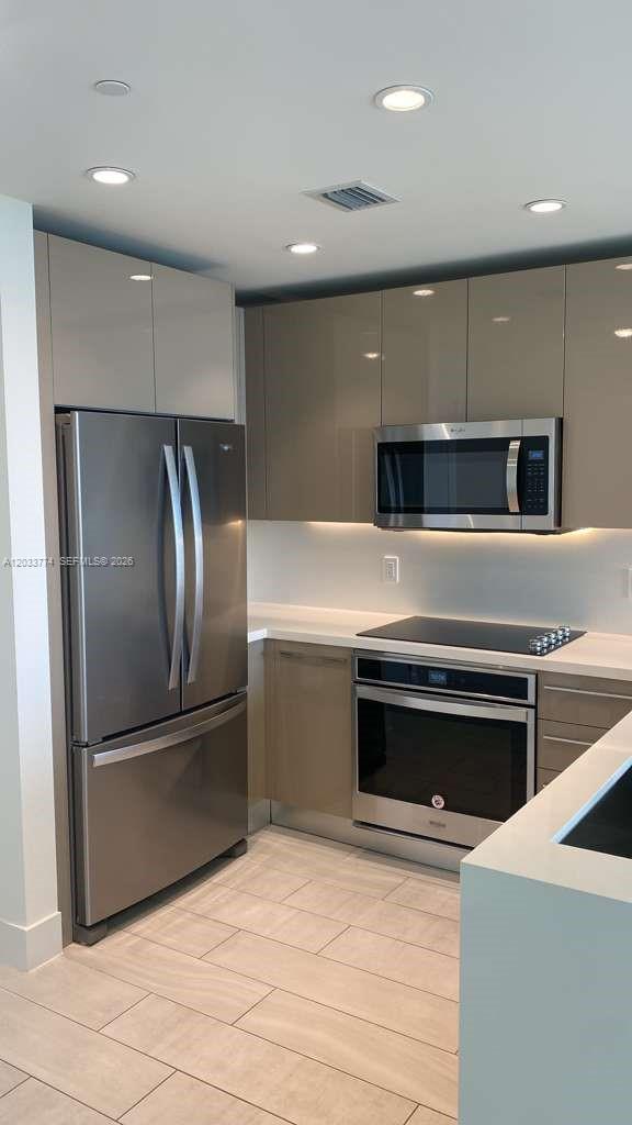 A modern kitchen features glossy taupe cabinets, stainless steel appliances, and light-colored tile flooring — 2000 Metropica Way # 2111, Sunrise FL 33323, SUNRISE, FL
