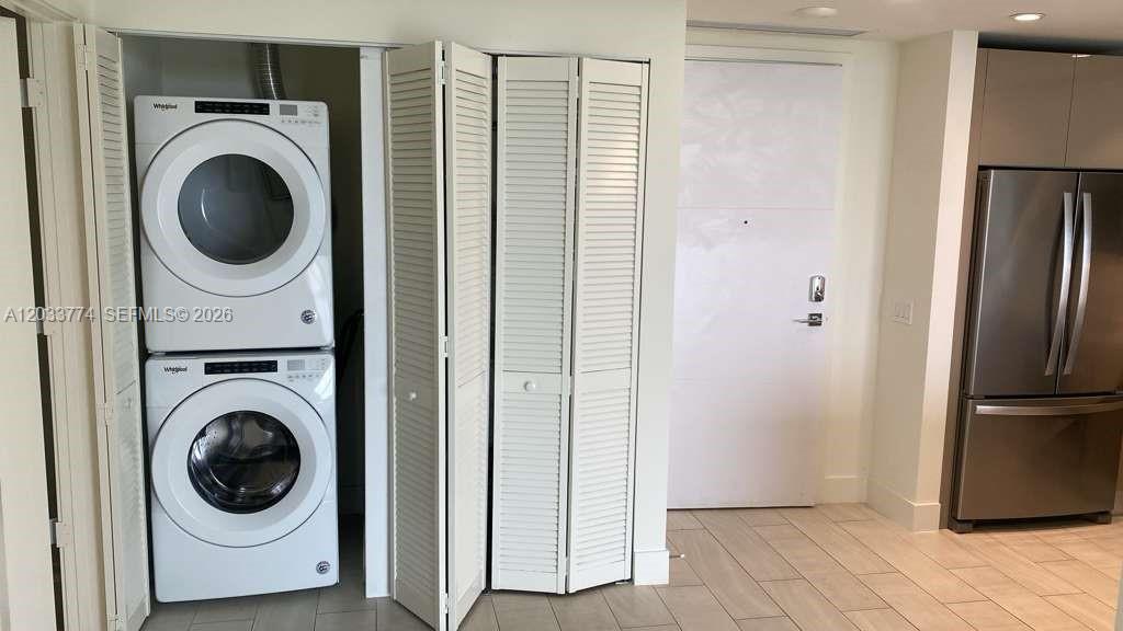 A stacked washer and dryer unit is located in a closet next to a refrigerator — 2000 Metropica Way # 2111, Sunrise FL 33323, SUNRISE, FL