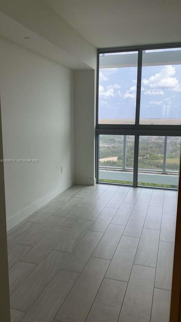 An empty room features light-colored wood-look tile flooring and floor-to-ceiling windows with a view — 2000 Metropica Way # 2111, Sunrise FL 33323, SUNRISE, FL