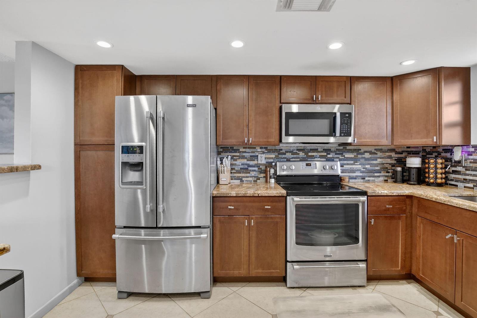 A kitchen features wood cabinets, stainless steel appliances, granite countertops, and a mosaic tile backsplash — 3001 W Rolling Hills Circle # 501, Davie FL 33328, DAVIE, FL