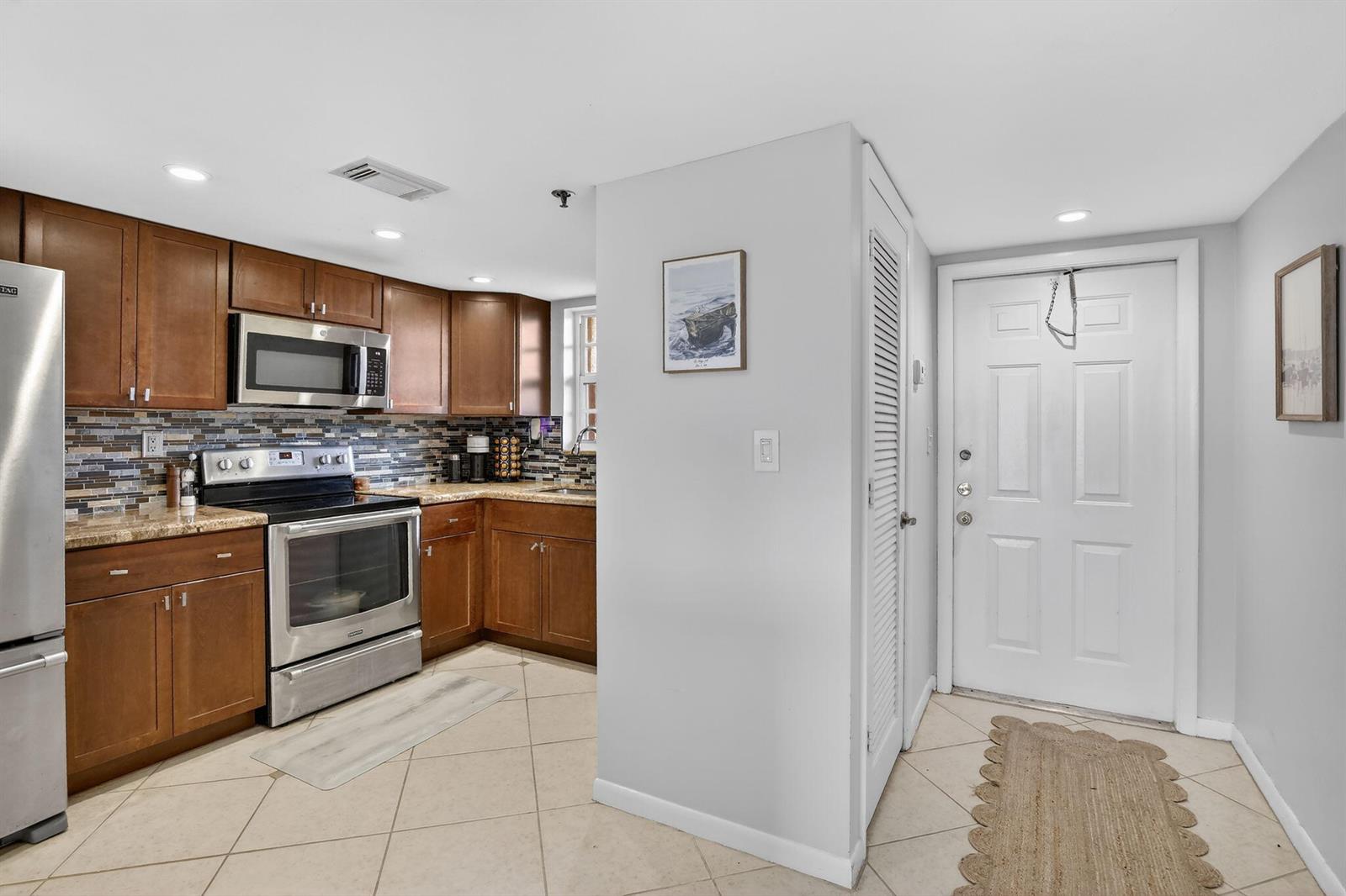 A kitchen with wood cabinets, stainless steel appliances, and tile flooring next to an entryway — 3001 W Rolling Hills Circle # 501, Davie FL 33328, DAVIE, FL