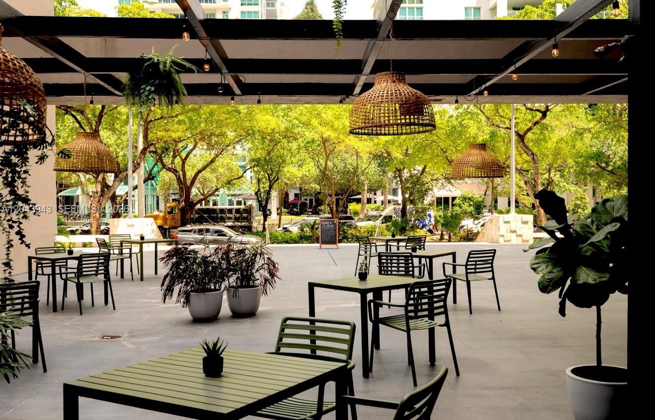 An outdoor patio area features metal tables and chairs under a pergola with hanging lights — 848 NE Brickell Avenue, Miami FL 33131, MIAMI, FL