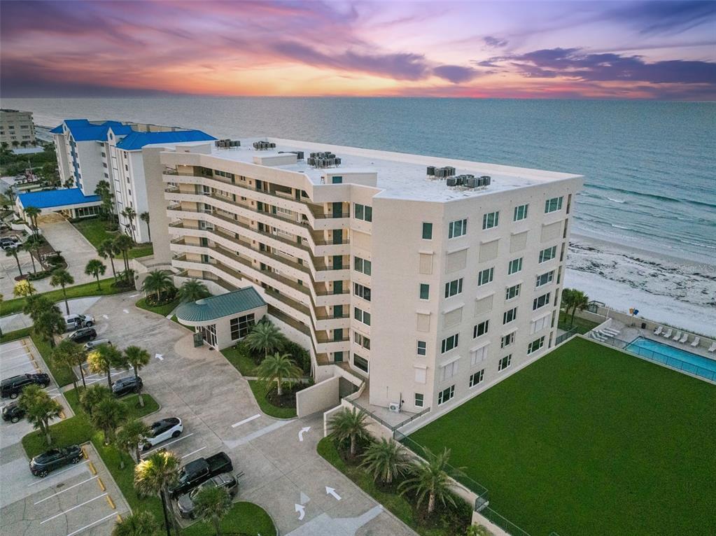 An aerial view shows a multi-story beachfront condominium building with a parking lot and pool — 4621 S ATLANTIC AVENUE UNIT 7702, PONCE INLET, FL
