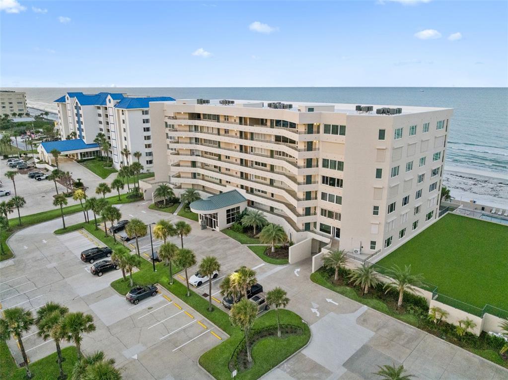 An aerial view shows a multi-story beachfront condominium building with a parking lot and palm trees — 4621 S ATLANTIC AVENUE UNIT 7702, PONCE INLET, FL