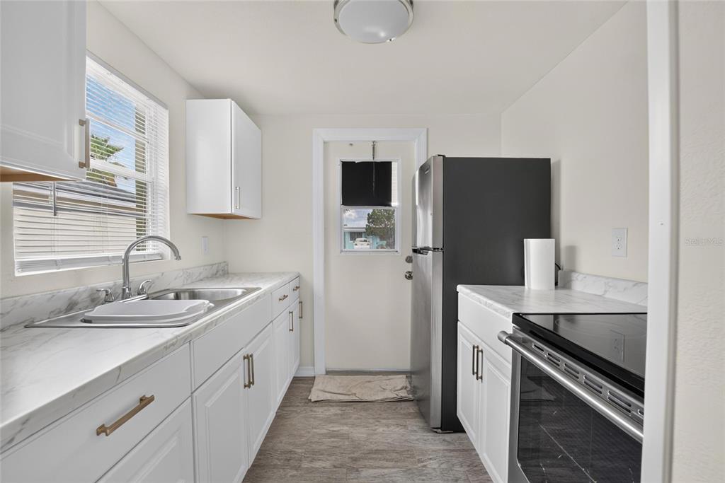 A galley kitchen features white cabinets, marble-look countertops, stainless steel appliances, and a back door — 4706 S 87TH STREET, TAMPA, FL
