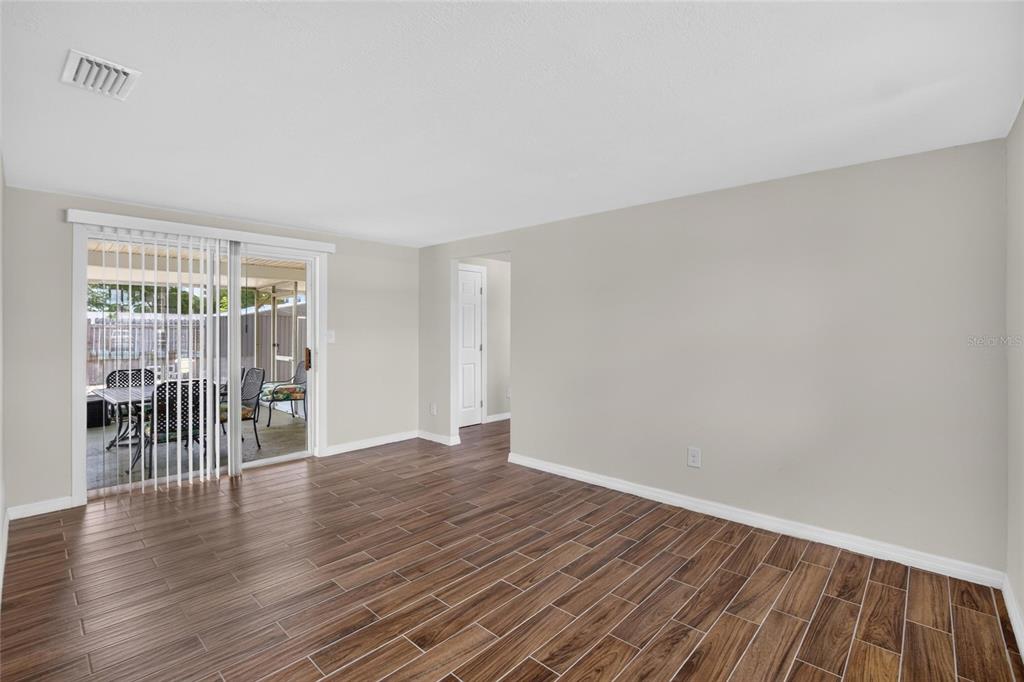 An empty room with wood-look tile flooring, light gray walls, and a sliding glass door — 4706 S 87TH STREET, TAMPA, FL