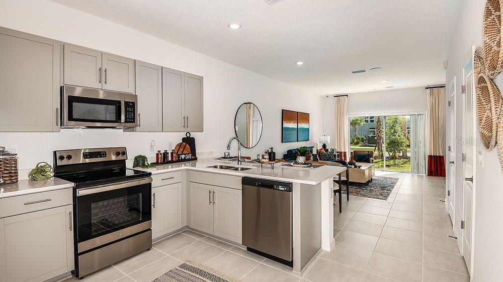 A modern kitchen features gray cabinets, stainless steel appliances, and a white quartz countertop island — 10601 ORBIT TERRACE, SARASOTA, FL