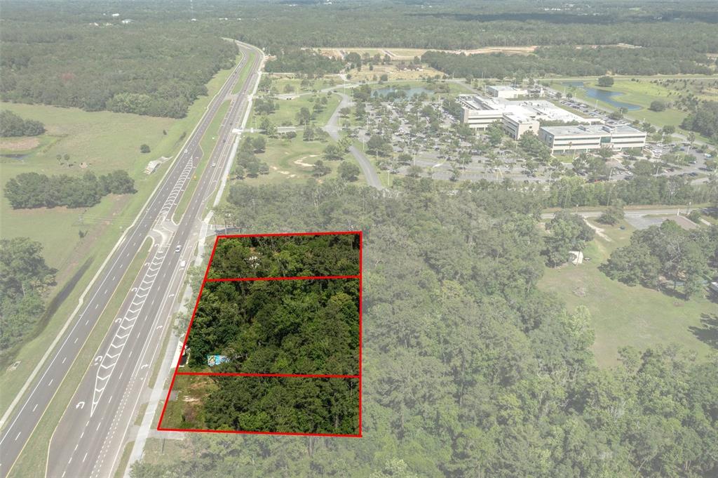 An aerial view shows three adjacent wooded lots bordering a multi-lane highway — 17166 CORTEZ BOULEVARD, BROOKSVILLE, FL