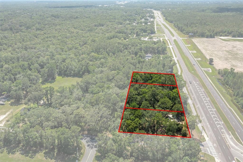 An aerial view shows a wooded plot of land outlined in red beside a highway — 17166 CORTEZ BOULEVARD, BROOKSVILLE, FL