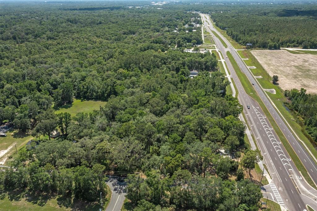 An aerial view shows a wooded lot adjacent to a multi-lane highway and open fields — 17166 CORTEZ BOULEVARD, BROOKSVILLE, FL