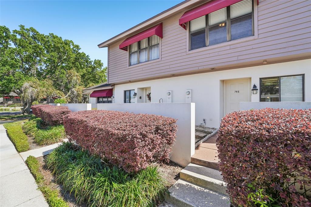 A two-story townhouse exterior features light-colored siding, red awnings, and a landscaped front yard — 745 OAK PARK PLACE, BRANDON, FL