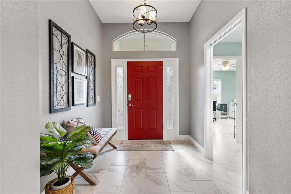 An entryway features a red front door, light tile flooring, and a bench with decor — 5852 ABNEY AVENUE, THE VILLAGES, FL