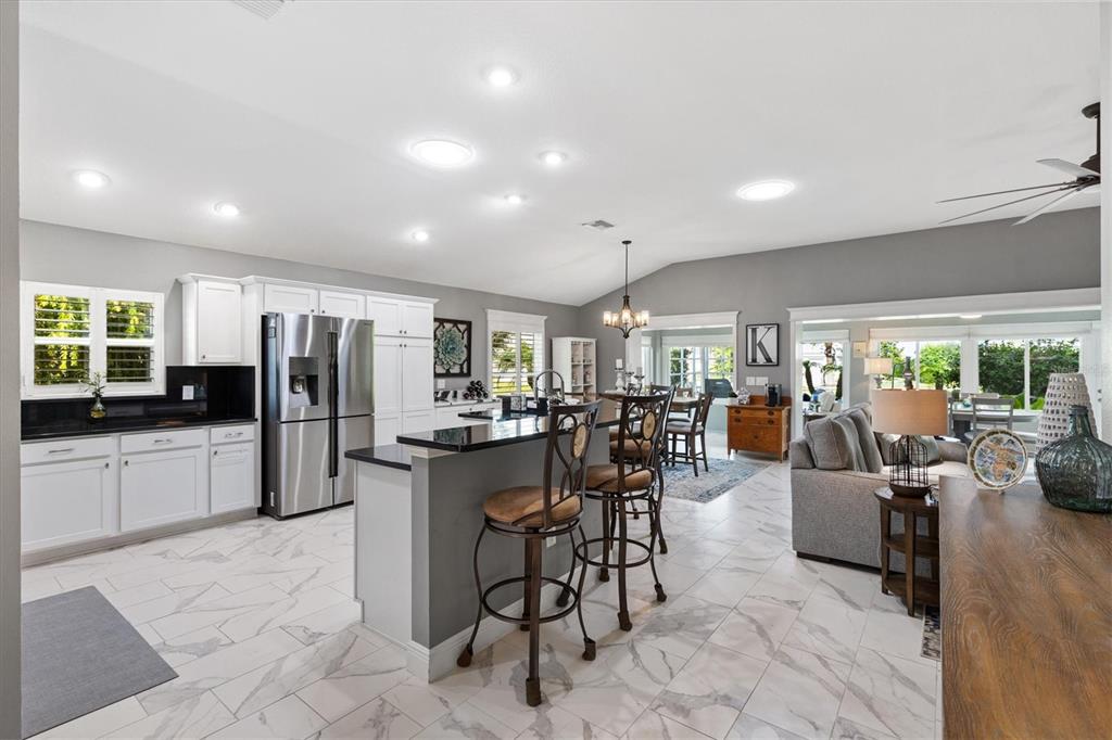 An open-concept kitchen features white cabinetry, a black island with bar stools, and marble-look flooring — 5852 ABNEY AVENUE, THE VILLAGES, FL