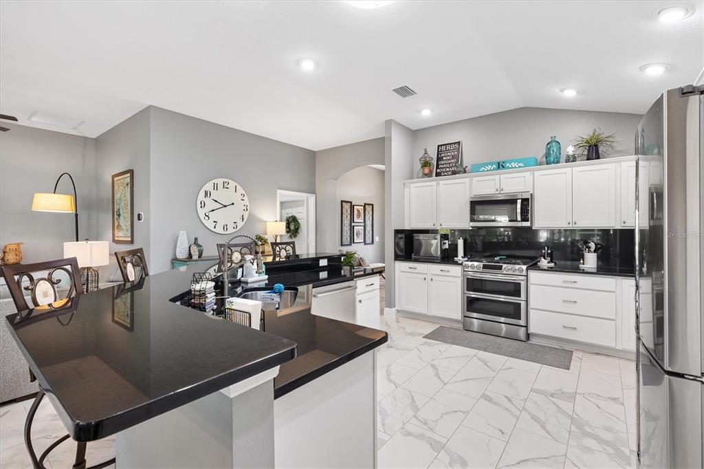 A modern kitchen features white cabinets, black countertops, stainless steel appliances, and white tile flooring — 5852 ABNEY AVENUE, THE VILLAGES, FL
