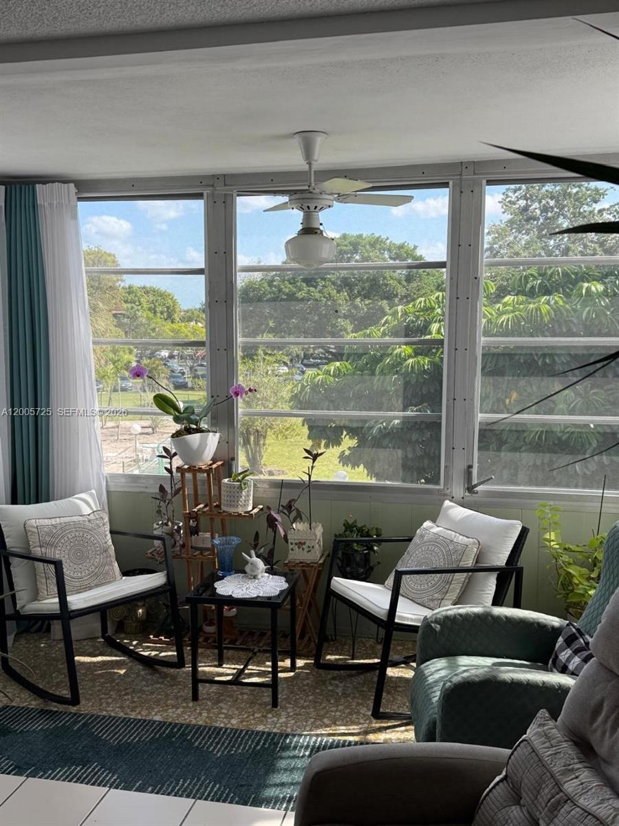A sunroom features two rocking chairs, a small table, potted plants, and large windows — 447 NE 195th St # 310, Miami FL 33179, MIAMI, FL