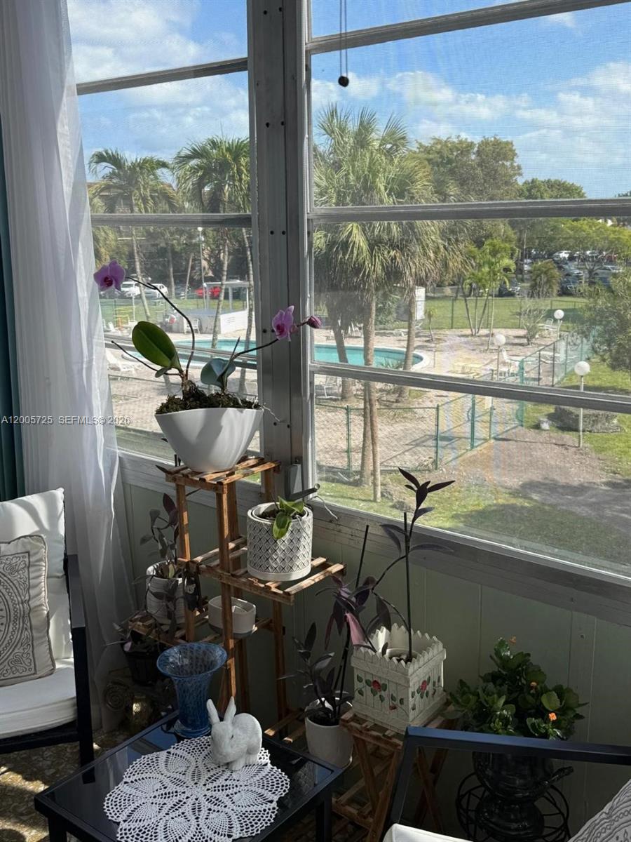 A sunroom features a tiered plant stand, potted orchids, and a view of a pool — 447 NE 195th St # 310, Miami FL 33179, MIAMI, FL
