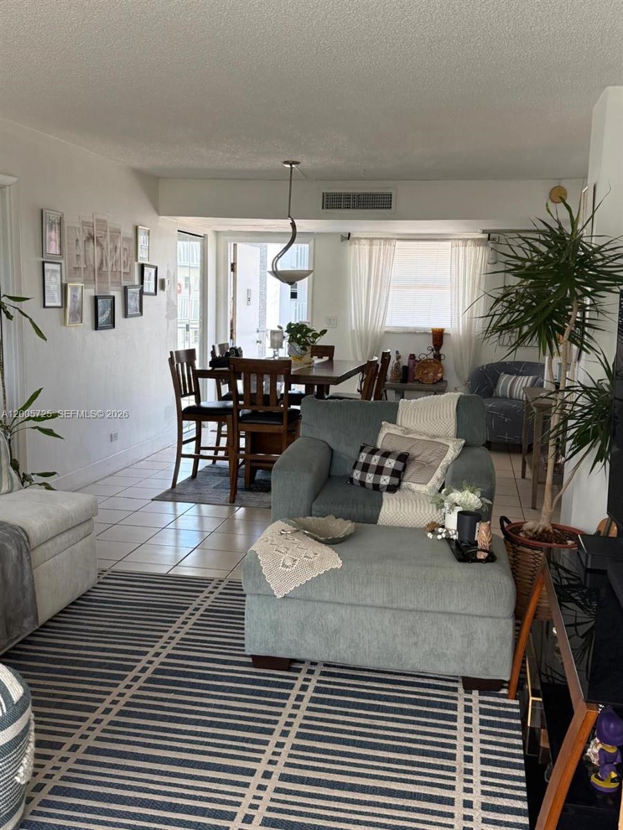 A living room with a blue armchair and ottoman leads to a dining area — 447 NE 195th St # 310, Miami FL 33179, MIAMI, FL