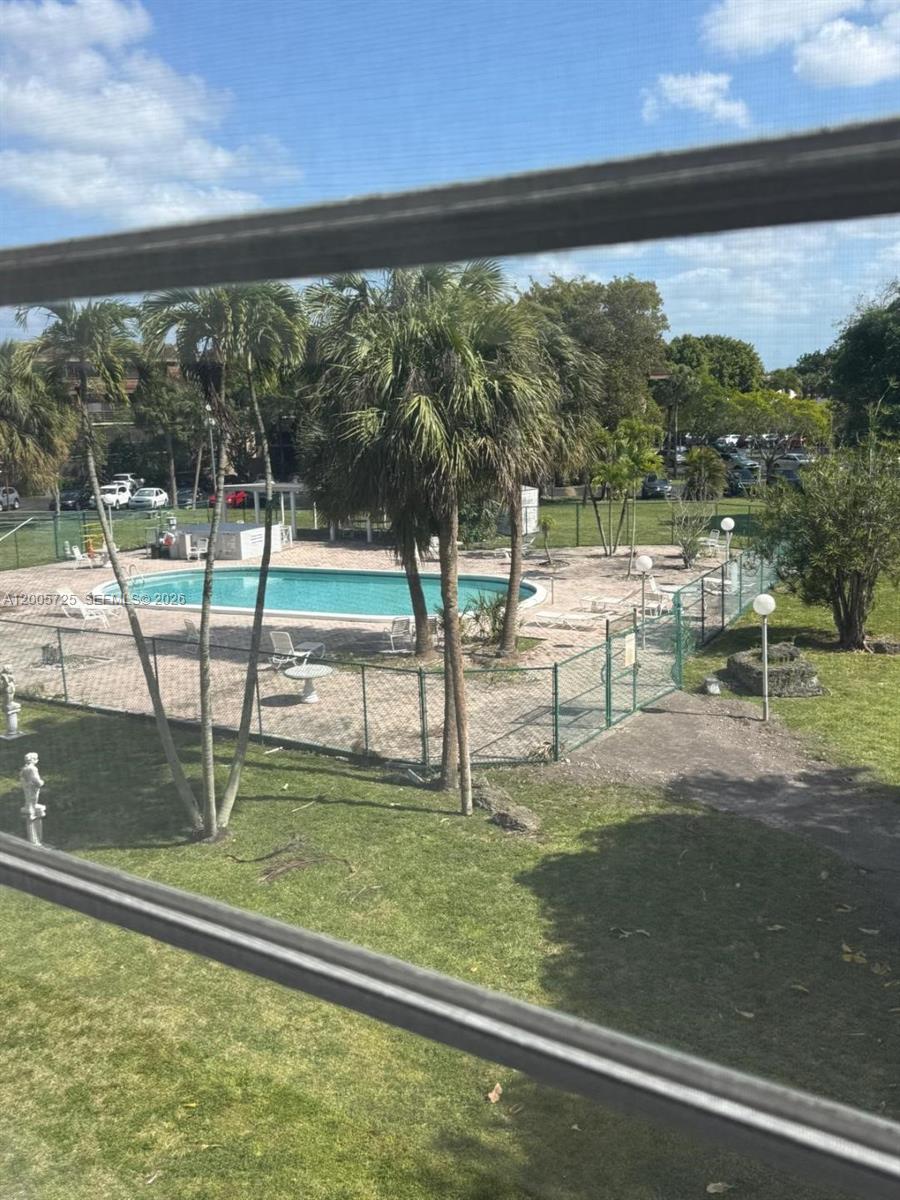 An outdoor swimming pool is enclosed by a chain-link fence surrounded by palm trees — 447 NE 195th St # 310, Miami FL 33179, MIAMI, FL