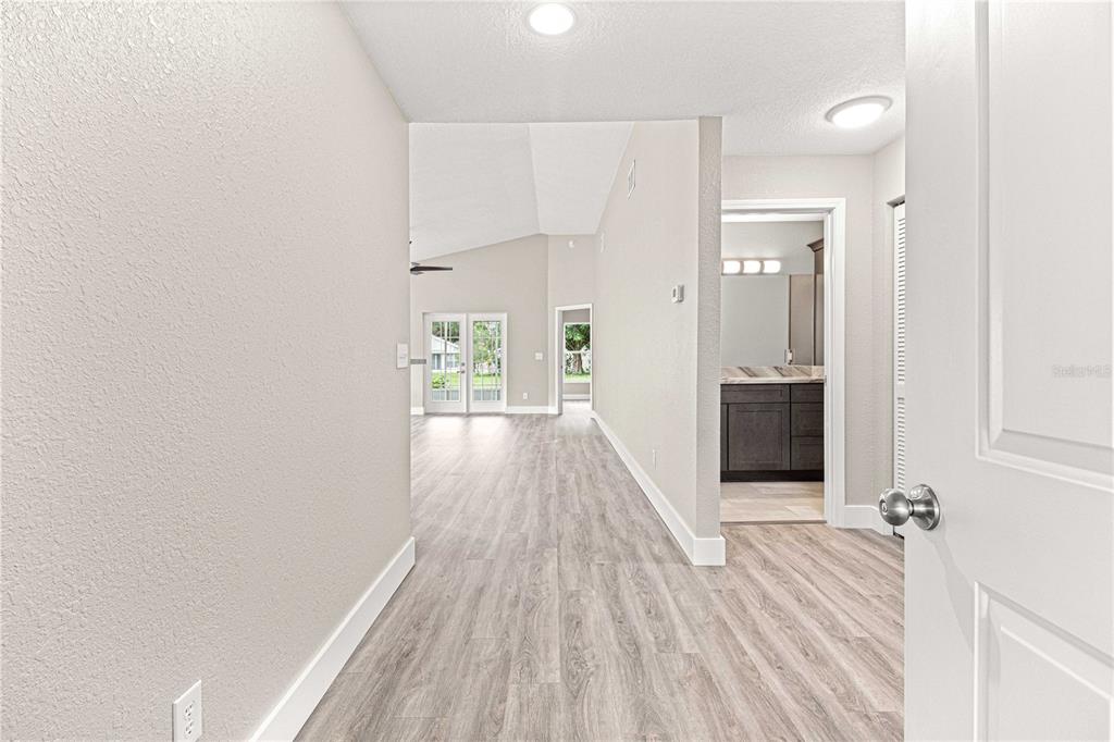A hallway with light wood-look flooring leads to a living area and a bathroom — 9270 SW 92ND PLACE ROAD, OCALA, FL