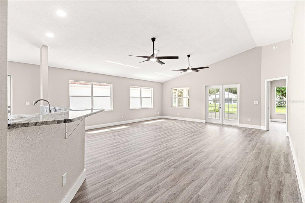 A spacious living area features light gray wood-look flooring, vaulted ceilings, and a kitchen island — 9270 SW 92ND PLACE ROAD, OCALA, FL