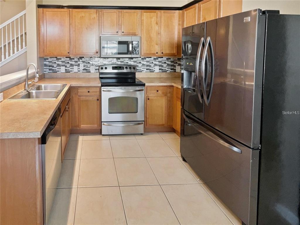 A kitchen features light wood cabinets, stainless steel appliances, a black refrigerator, and tile flooring — 4970 SW 45TH STREET, OCALA, FL