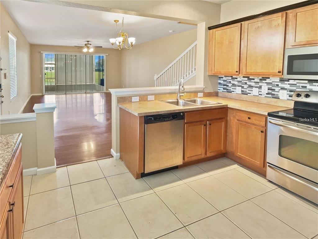 A kitchen with light wood cabinets and stainless steel appliances overlooks an open living area — 4970 SW 45TH STREET, OCALA, FL