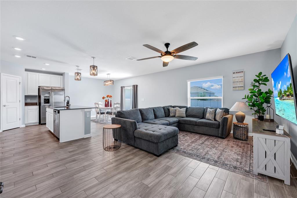 An open-concept living room and kitchen feature gray wood-look tile flooring and a sectional sofa — 6939 WILSON PASTURE AVENUE, GROVELAND, FL