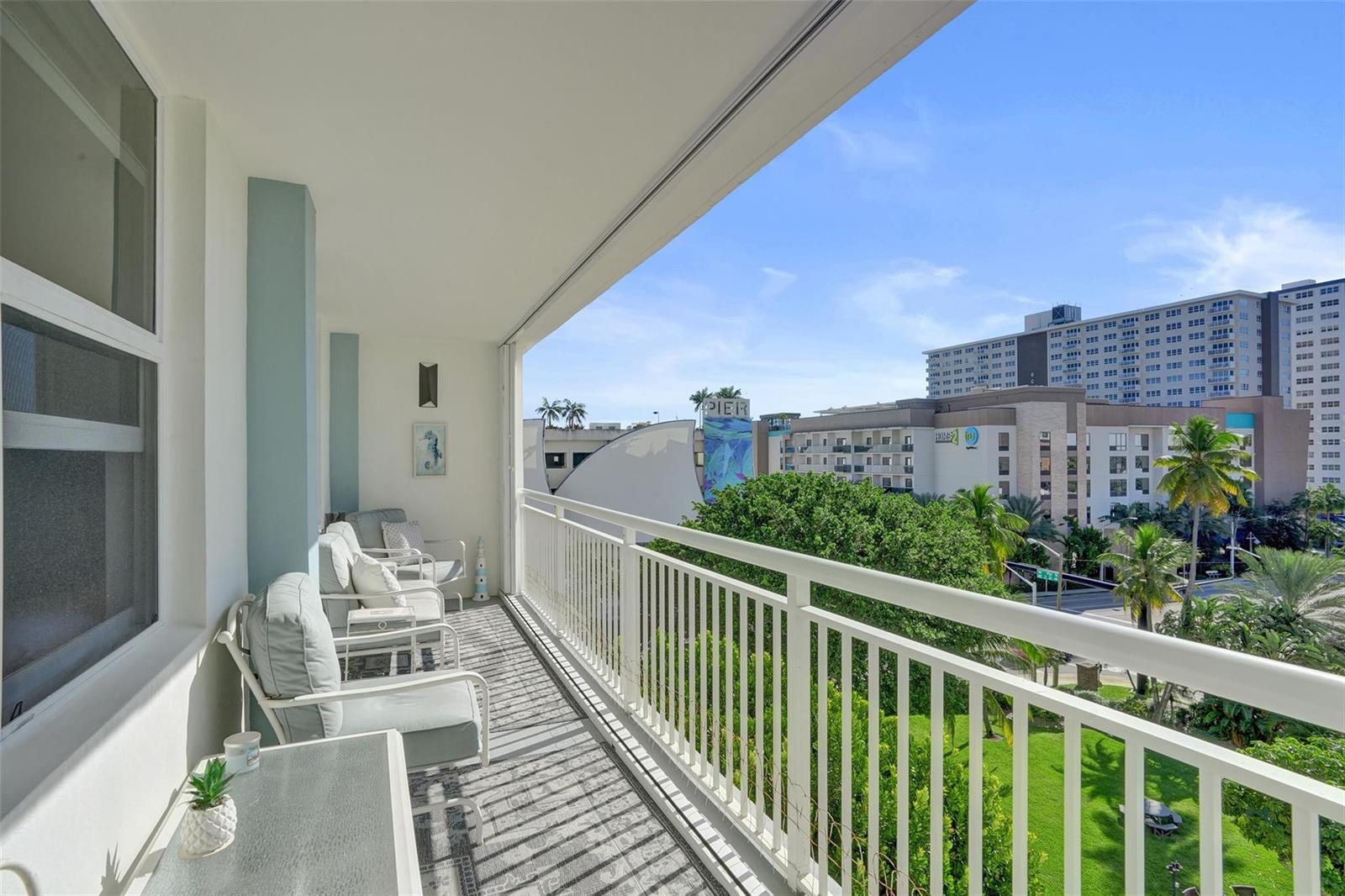 A balcony with white railings, outdoor seating, and a view of nearby buildings and trees — 201 N Ocean Boulevard # 603, Pompano Beach FL 33062, POMPANO BEACH, FL
