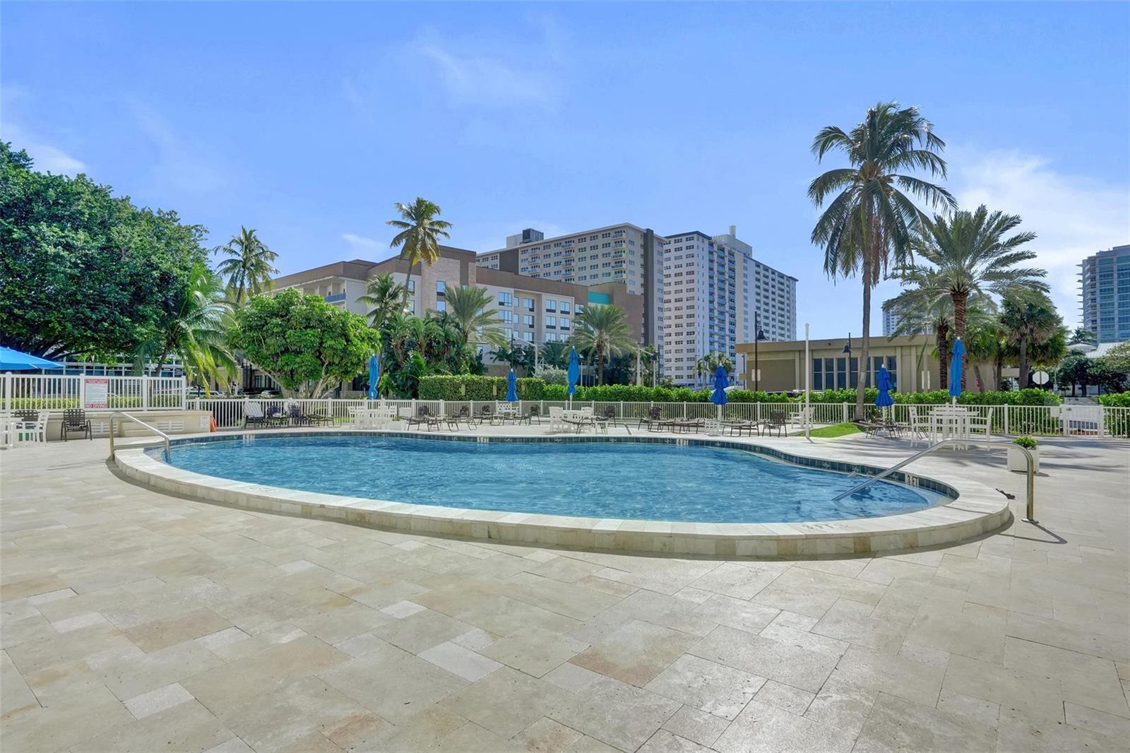 An outdoor swimming pool surrounded by a stone patio, palm trees, and multi-story buildings — 201 N Ocean Boulevard # 603, Pompano Beach FL 33062, POMPANO BEACH, FL