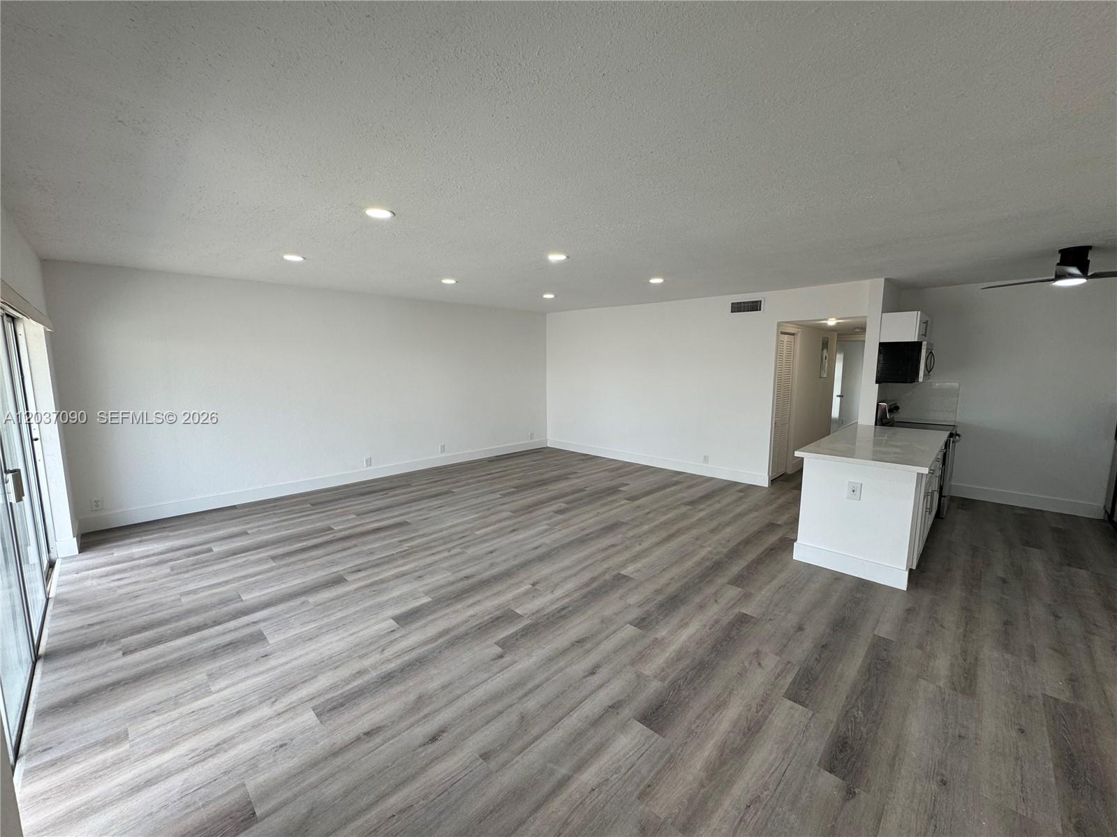 An open-concept living area features light gray wood-look flooring and a white kitchen island — 630 Layne Blvd # 211, Hallandale Beach FL 33009, HALLANDALE BEACH, FL